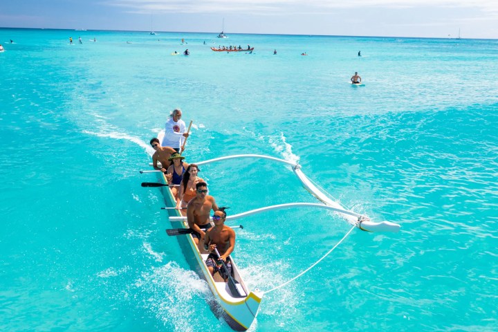Group rowing canoe on clear turquoise waters, sunny day.
